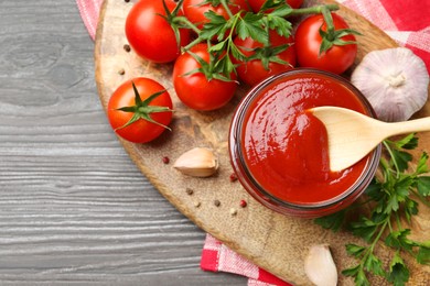 Photo of Tasty ketchup, fresh tomatoes, parsley and spices on grey wooden table, flat lay. Space for text