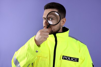 Photo of Policeman looking through magnifier glass on violet background