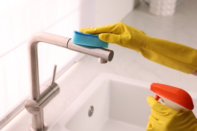Photo of Woman cleaning faucet with sponge and detergent in kitchen, closeup
