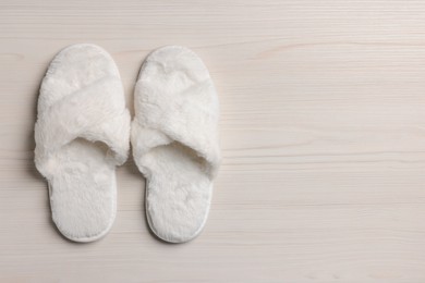 Photo of Pair of soft slippers on white wooden floor, top view. Space for text