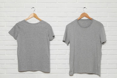 Photo of Hangers with blank t-shirts on white brick wall. Mock up for design