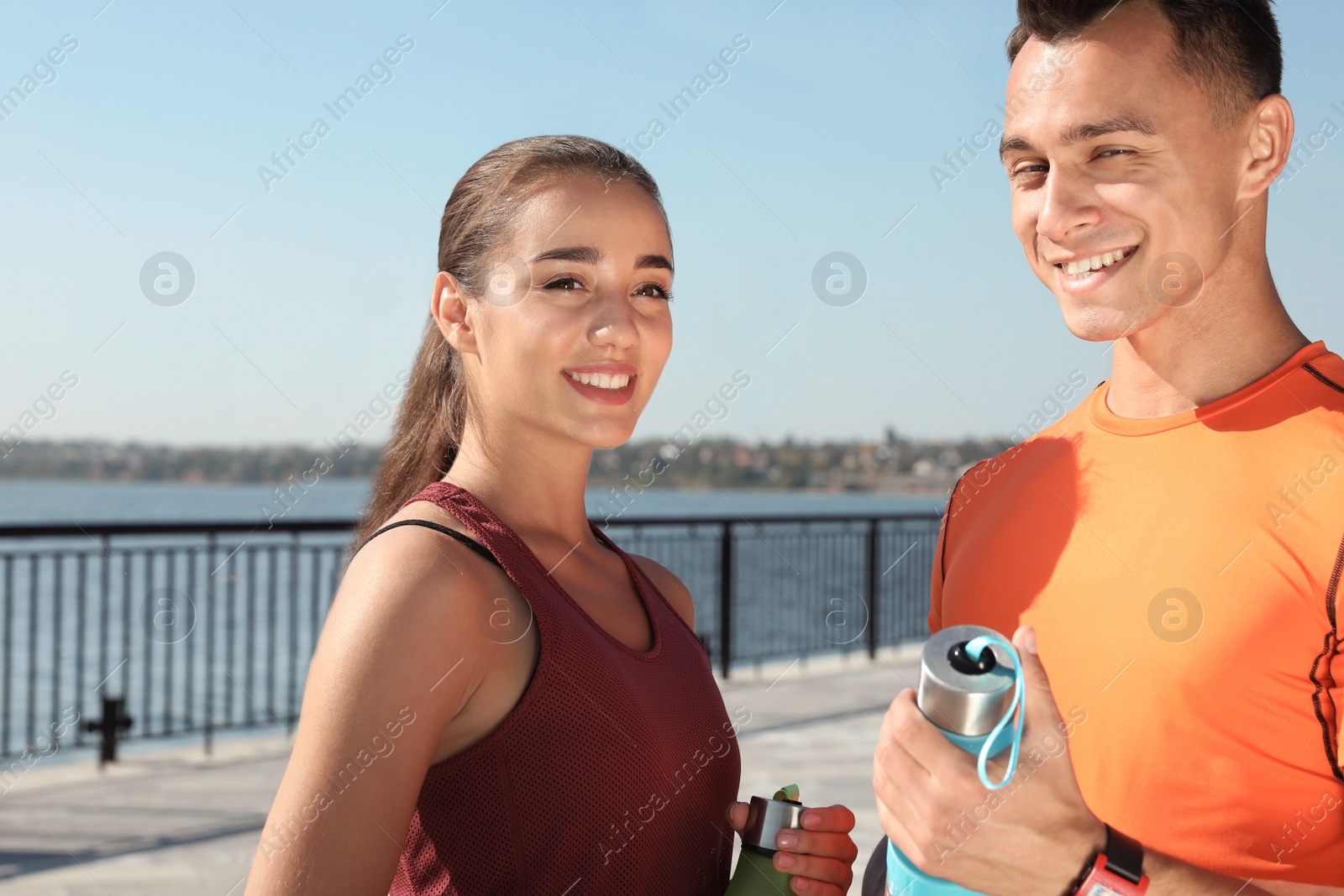 Photo of Young sporty couple with bottles of water outdoors on sunny day