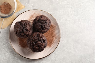 Photo of Delicious chocolate muffins and cacao powder on light grey table, flat lay. Space for text