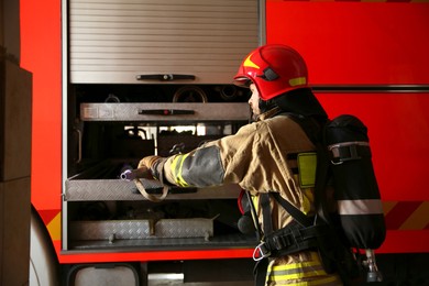 Photo of Firefighter in uniform with safety equipment near fire truck at station