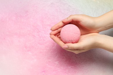 Woman holding bath bomb over water with foam, top view. Space for text