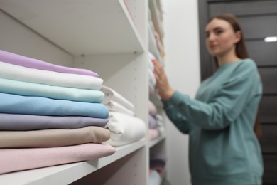 Photo of Stack of bed linens on shelf in shop. Customer choosing bedding indoors, selective focus