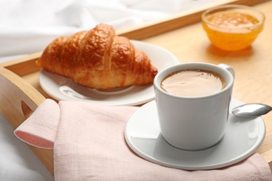 Photo of Cup of aromatic coffee, croissant and jam on wooden tray, closeup. Breakfast in bed