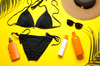 Photo of Flat lay composition with black swimsuit and beach accessories on yellow background