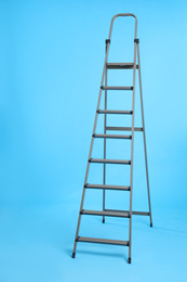 Photo of Metal stepladder on light blue background. Construction tool