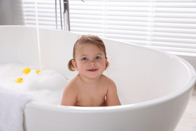 Photo of Cute little girl taking bubble bath with toys indoors