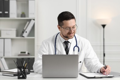 Photo of Doctor having online consultation via laptop at table in clinic