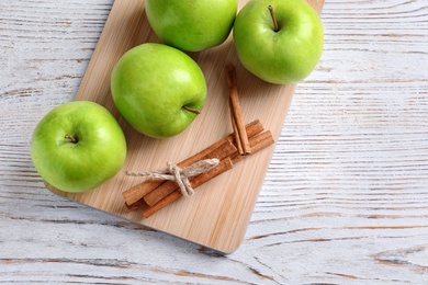Photo of Fresh apples and cinnamon sticks on wooden board, top view