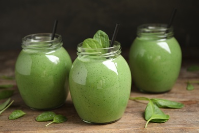 Photo of Jars of healthy green smoothie with fresh spinach on wooden table