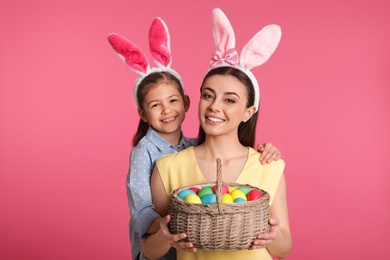 Photo of Mother and daughter in bunny ears headbands with Easter eggs on color background
