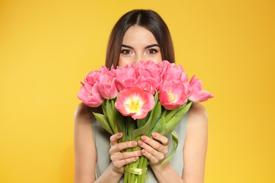 Photo of Beautiful girl with spring tulips on yellow background. International Women's Day