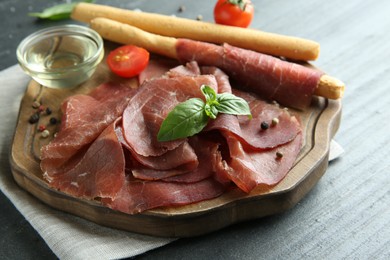 Photo of Delicious bresaola, tomato, grissini sticks and basil leaves on grey textured table, closeup