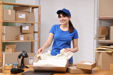 Photo of Post office worker packing parcel at wooden table indoors