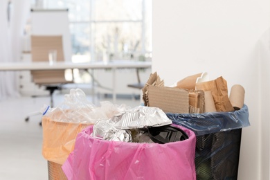 Photo of Full trash cans in modern office, space for text. Waste recycling