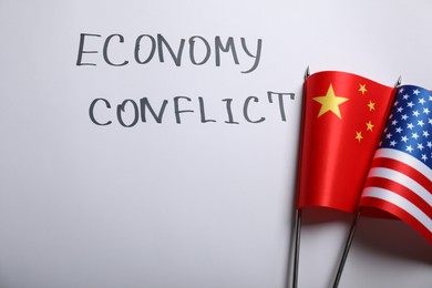 Photo of USA and China flags near words ECONOMY CONFLICT on white background, flat lay