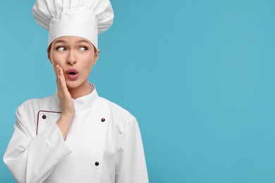 Photo of Happy woman chef in uniform on light blue background, space for text