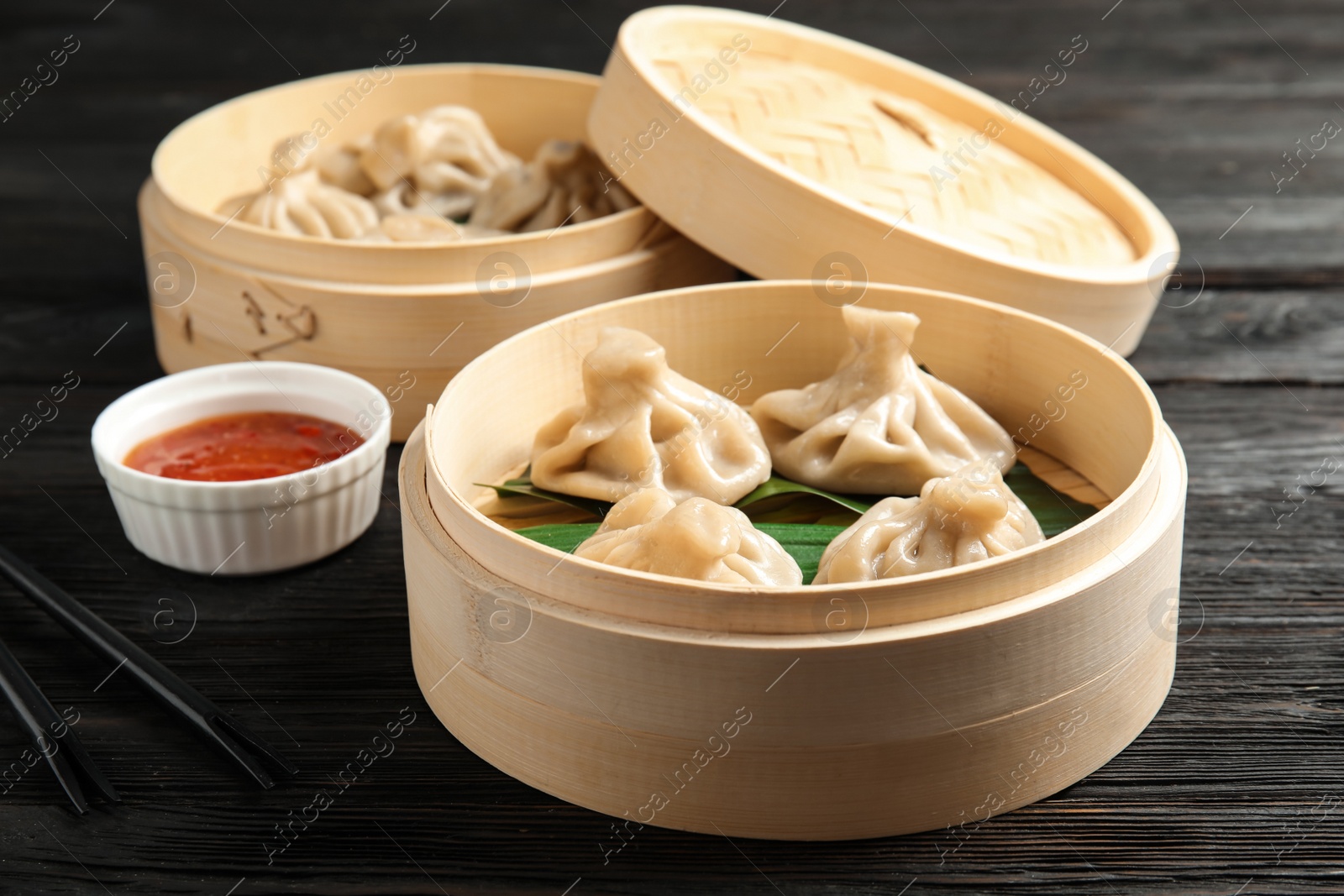 Photo of Bamboo steamer with leaves and tasty baozi dumplings on table