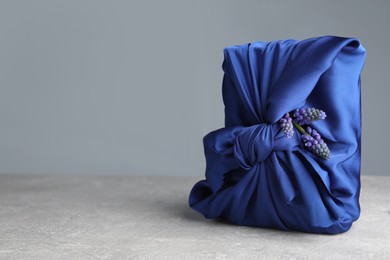 Photo of Furoshiki technique. Gift packed in blue silk fabric and muscari flowers on light grey table. Space for text