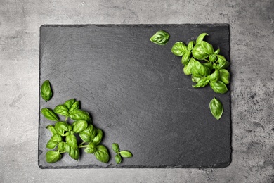 Photo of Slate plate with fresh basil leaves and space for text on table, top view