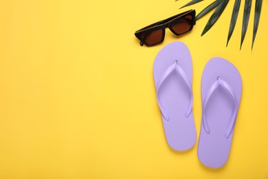 Photo of Stylish light purple flip flops, sunglasses and palm leaf on yellow background, flat lay. Space for text