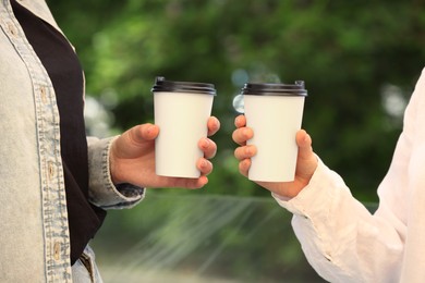 Photo of Women holding takeaway paper cups outdoors, closeup. Coffee to go