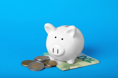 Photo of Ceramic piggy bank, euro banknote and coins on light blue background. Financial savings