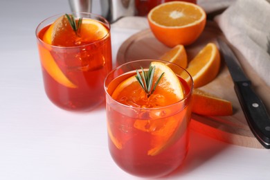 Photo of Aperol spritz cocktail, rosemary and orange slices on white table, closeup