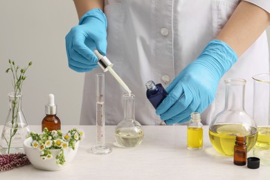 Scientist developing cosmetic oil at white wooden table, closeup