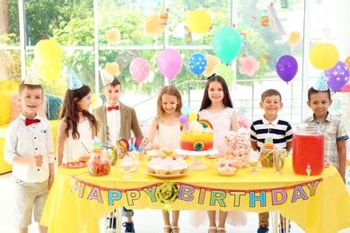 Photo of Cute children near table with treats at birthday party indoors
