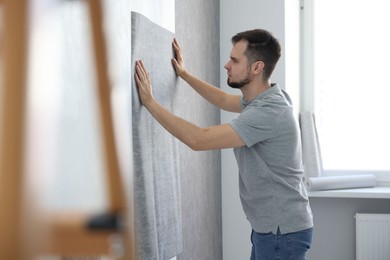 Photo of Man hanging stylish gray wallpaper in room