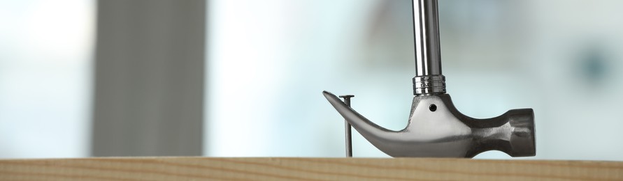 Image of Hammer pulling metal nail out of wooden surface against blurred background indoors, space for text. Banner design