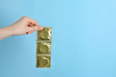 Photo of Woman holding condoms on light blue background, closeup. Space for text
