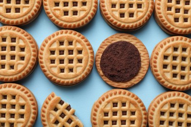 Photo of Tasty sandwich cookies with cream on light blue background, flat lay