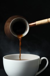 Photo of Turkish coffee. Pouring brewed beverage from cezve into cup against black background