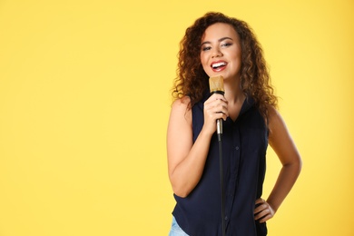 Photo of Portrait of curly African-American woman posing with microphone on color background. Space for text