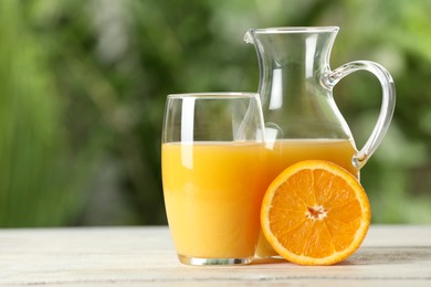 Photo of Tasty orange juice in glass and jug on white wooden table against blurred background. Space for text