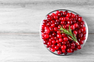 Photo of Fresh ripe cranberries and rosemary in bowl on grey wooden table, top view. Space for text