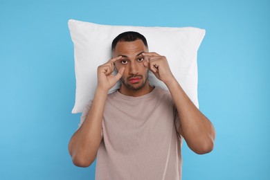 Photo of Tired man with pillow on light blue background. Insomnia problem