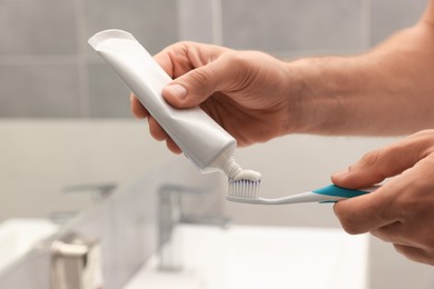 Photo of Man applying toothpaste on brush in bathroom, closeup