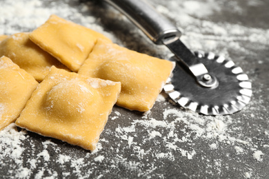 Photo of Ravioli and cutter on grey table, closeup. Italian pasta