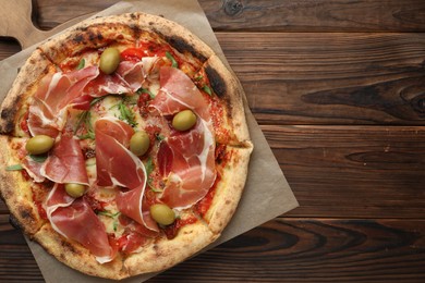 Photo of Tasty pizza with cured ham, olives and sun-dried tomato on wooden table, top view. Space for text