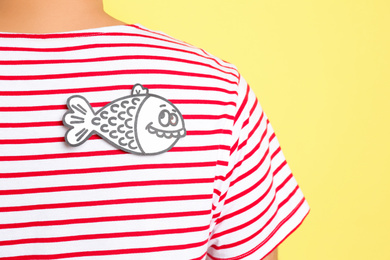 Photo of Man with paper fish on back against yellow background, closeup. April fool's day
