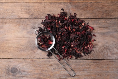 Photo of Dry hibiscus tea and sieve on wooden table, flat lay