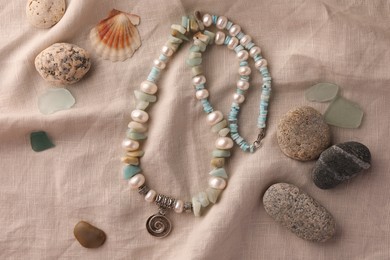 Photo of Beautiful necklace with gemstones, different stones and seashell on light cloth, flat lay