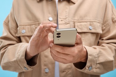 Photo of Young man sending message via smartphone on light blue background, closeup