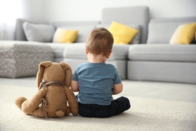 Photo of Little boy with toy sitting on floor in living room. Autism concept